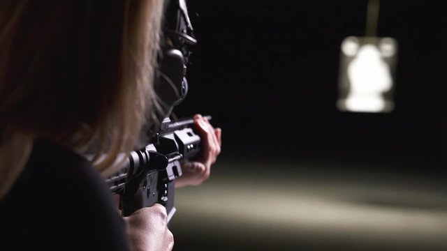 Woman aiming a automatic firearm rifle at a shooting range, closeup