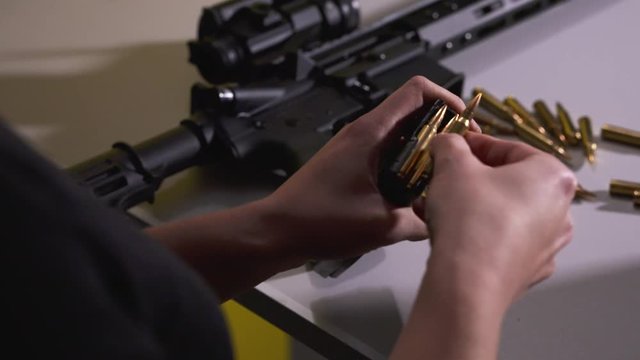 Young Female Reloading Rifle Bullets into a Magazine while Rifle and Bullets Sit on the Table Beside her Inside a Shooting Range in Slow Motion