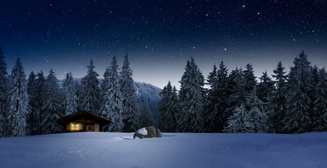 Gemütliche Holzhütte mit Beleuchtetem Fenster in Wnterwald bei Nacht im Winter