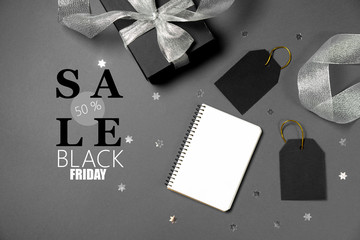 Black friday sale concept. Black paper boxes with silver ribbon, price tags, notebook, stars confetti and text on gray background. Flat lay, top view, copy space
