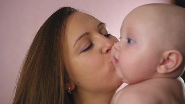 Mother and Baby. Happy young mother hugs baby and kisses on chubby cheeks at home. Close up shot.