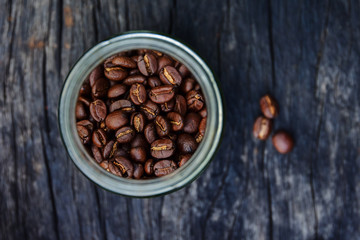 Fototapeta premium roasted coffee beans in glass containers on old wood table background, overhead view with copy space