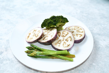 Healthy eating concept. Steamed vegetables in a white plate on a blue table. Eggplant, broccoli, asparagus.