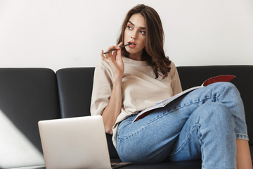 Image of woman studying with exercise book and laptop on sofa in apartment
