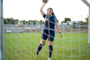 woman with the ball in her hands, on the green grass, football field, through the net gate