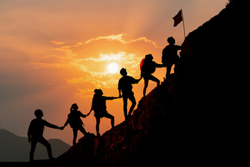 Silhouette of people helping each other hike up a mountain at sunset background. Hiking, Business, teamwork, success, help and goal concept. - obrazy, fototapety, plakaty
