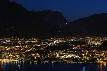 Evening panoramic view of the of Riva Del Garda, Lake Garda. City night lights reflected in water. Aerial view of the city of Riva del Garda