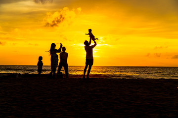 mother and father carry a child to take a photo on the beach in golden sunset.