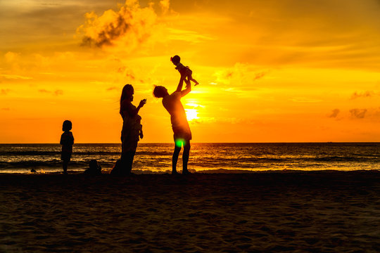 mother and father carry a child to take a photo in golden sunset at Kata beach Phuket Thailand