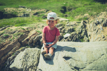 Naklejka premium Toddler sitting on rock with a piece of charcoal