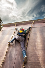 Young boy in wellys climbing up a wall with ropes