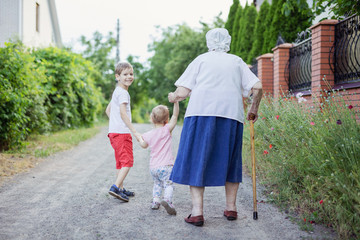 Young boy, toddler girl and their great grandmother walking  down street in countryside