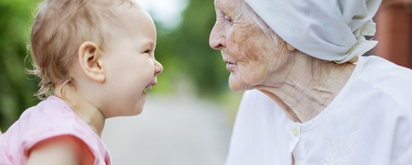 Happy toddler girl and her great grandmother looking at one another, laughing and talking outdoors