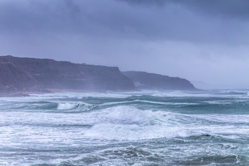 Fototapeta na wymiar A huge ocean waves breaking on the coastal cliffs in at the cloudy stormy day. Breathtaking romantic seascape of ocean coastline.