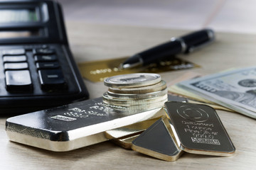 A pile of silver bars and coins, dollar bills, gold credit card, pen and a calculator.