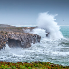 A huge ocean waves breaking on the coastal cliffs in at the cloudy stormy day. Breathtaking romantic seascape of ocean coastline. Peniche, Portugal.