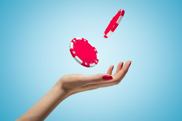 Female hand throwing two red casino tokens up in the air on blue background