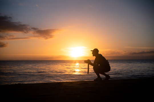 The silhouette of a male hobbyist photographer taking photos of a beautiful colorful sunset on the West Puerto Rico coast near Rincon