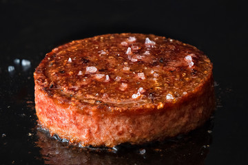 Plant based vegetarian burger patty with rock salt being cooked on flat black iron grill.