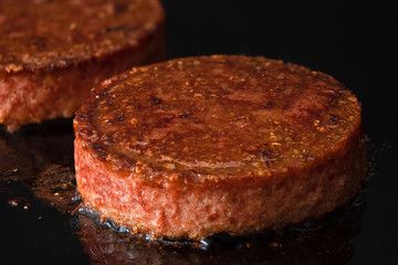 Plant based vegetarian burger patties being cooked on flat black iron grill.