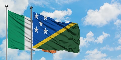 Ireland and Solomon Islands flag waving in the wind against white cloudy blue sky together....