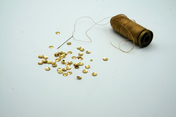 Gold sequins, spool of golden thread, needle on rippled on white background. Sewing and decorating...