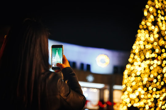 woman takes pictures of Christmas tree outside. holiday background, Christmas lights. Copy space for your text