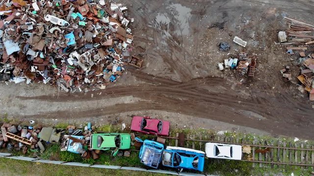 Aerial flight over a small industrial warehouse for the recycling and disposal of old cars and scrap metal. Piles of old broken rusty cars stacked in scrapyard. Aerial shot taken by drone