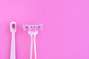 pink disposable razor for safe shaving of female skin and toothbrush with selective focus on purple background. Woman Razor and toothbrush on bright backdrop. Sharp razor for personal hygienic routine