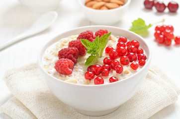 Tasty oatmeal porridge with raspberries and red currant in bowl