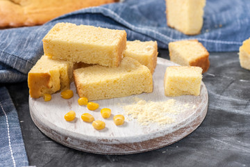 Freshly baked corn bread on a round wooden white board with corn on a dark background with napkin. Traditional pastries in US national cuisine.
