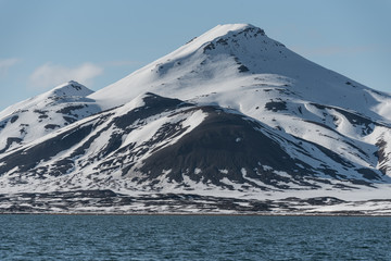 Snow covered mountains with rocky slopes by an arctic fjord in Svalbard