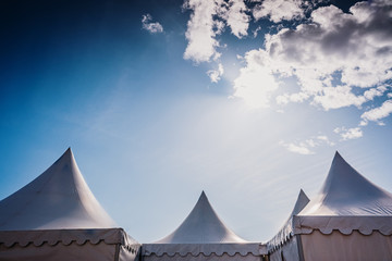 Peaks of three pyramidal white tents and blue sky background with space for advertisers text. - obrazy, fototapety, plakaty