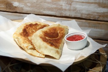 Cheburek and adjika on white paper on wooden background