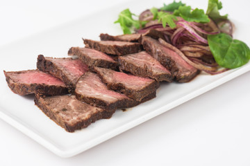 Plate with meat cutting and fresh greens on white plate