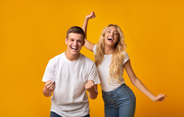 Obraz premium Happy millennial couple celebrating success on yellow background