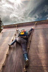 Young boy in wellys climbing up a wall with ropes