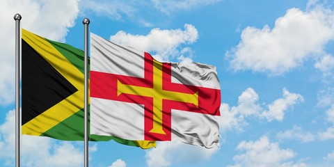 Jamaica and Guernsey flag waving in the wind against white cloudy blue sky together. Diplomacy concept, international relations.