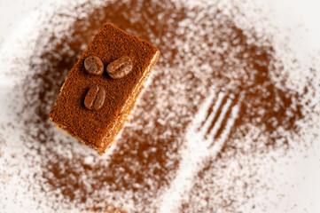 Slice of tiramisu cake decorated with coffee beans on top on a white plate