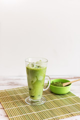 Iced matcha latte drink in tumbler glass with coconut milk pouring from pitcher by hand, copy space.