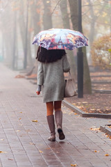 Morning fog in town in the fall. A woman with a colored umbrella is walking along the alley....