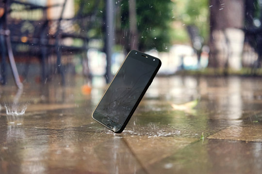  Smartphone falling and crashing on wet ground in the city park on a rainy day