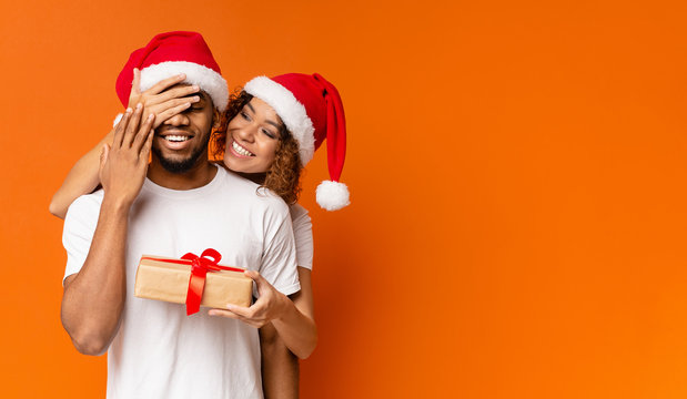 Black millennial couple with Christmas gift on orange background