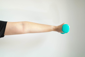 A close-up image of the left hand and arm of a woman lifting dumbbells weighs 1 kilogram in...