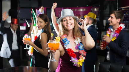 Portrait of young cheerful women and men in caps with cocktails