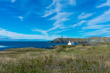 church on rocky cliff by the sea with lighthouse in the background