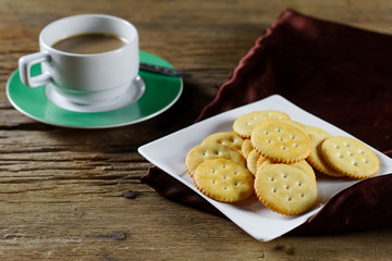 Round cracker on white plate and coffee cup on wood background