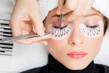 Eyelash extension procedure. Master tweezers fake long lashes beautiful female eyes - obrazy, fototapety, plakaty