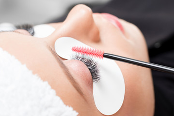 Eyelash extension procedure. Woman master combs lashes