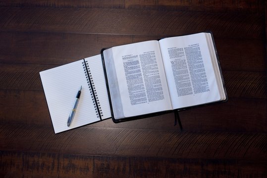 Overhead Shot Of An Open Bible Near A Notebook On A Wooden Surface